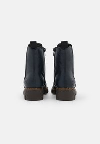 Bottes de cheville en cuir bleu foncé avec une finition lisse, des fermetures éclair sur les côtés et des semelles en caoutchouc marron avec un motif texturé.