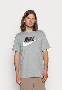Hallikas puuvillane T-särk, millel on suur must Nike logo ja valge sirm. Lühikesed varrukad, mugav lõige ja ümar kaelus.