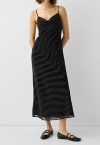 Czarna sukienka midi w białe kropki, z cienkimi regulowanymi ramiączkami i dekoltem typu cowl. Gładki materiał o zwiewnym kroju.