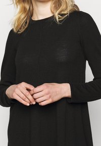 Pullover nero a maglia con maniche lunghe, dotato di scollatura rotonda e vestibilità morbida. Si notano leggere texture e dettagli delle cuciture.