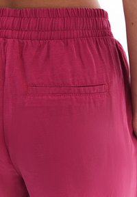 Fuksiapinkit housut, joissa on joustava vyötärö, takatasku ja sileä, hieman rakenteellinen kangas.