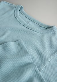 Lyseblå T-shirt med ribstruktur, rund hals og korte ærmer, lavet af blødt stof med subtil tekstur og syningsdetaljer.