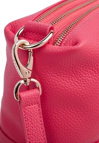 Różowa torba skórzana o teksturowanej powierzchni, z złotymi zamkami i elementami metalowymi. Posiada klips oraz płaski pasek. Okrągły kształt o gładkim wykończeniu.