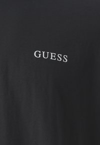 Fekete pamut póló, a bal oldalon egy kis fehér "GUESS" logóval. Simaság és klasszikus kerek nyakú dizájn jellemzi.