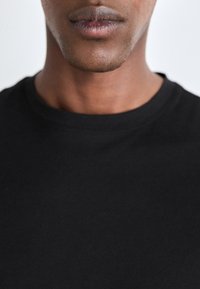 Camiseta de algodón negra con cuello redondo, diseño sencillo y mangas cortas, que muestra una textura suave y una estética simple.