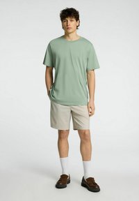 Svetle zelené tričko s krátkým rukávem v kombinaci s béžovými šortkami, bílými ponožkami a hnědými botami. Jednoduchý design, měkká textura a pohodlný střih.