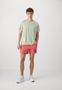 Lys grøn Nike t-shirt med korte ærmer; stærkt lyserøde shorts med sidelommer. Hvide sportsko. Enkel, moderne design.