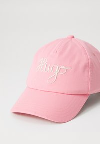 Roze cap van katoen, met een gebogen klep en geborduurd "Hugo"-logo in het wit. Glad oppervlak met zichtbare stikdetails.