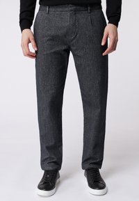 Ciemnoszare, strukturalne spodnie o dopasowanym kroju, z kieszeniami z przodu i elastycznym pasem. Połączone z czarnymi sneakersami.