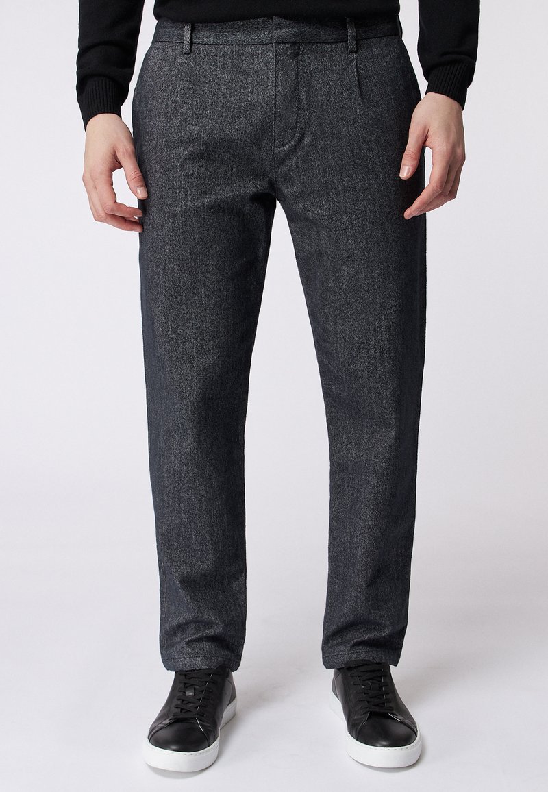 Ciemnoszare, strukturalne spodnie o dopasowanym kroju, z kieszeniami z przodu i elastycznym pasem. Połączone z czarnymi sneakersami.