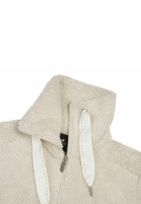 Beige fleece-takki, jonka kauluksessa on osittain avattu vetoketju ja valkoiset narut, joissa lukee "Luhtra".