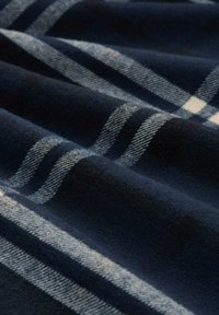 Pătură în carouri bleumarin, cu un material moale și texturat. Prezintă dungi albe și albastre deschise într-un model quadriculat.