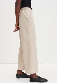 Beige wijde broek met een elastische tailleband, met een soepele textuur en zijzakken. Gecombineerd met zwarte instapschoenen.