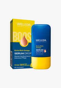 Flacone e scatola del siero extra ricco Omega di Weleda in blu e giallo, con olio di avocado e omega 3-6-9 per la cura della pelle.