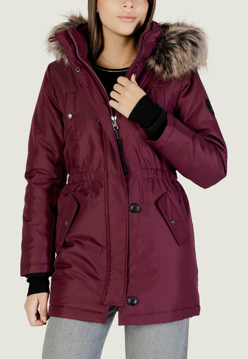 Giacca parka bordeaux con cappuccio in pelliccia sintetica, vita regolabile con coulisse e chiusura lampo davanti. Presenta tasche con bottoni e polsini a coste. Texture liscia.