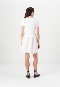 White ribbed top with short sleeves, paired with a white eyelet skirt featuring scalloped hem. Black lace-up flats complete the outfit.