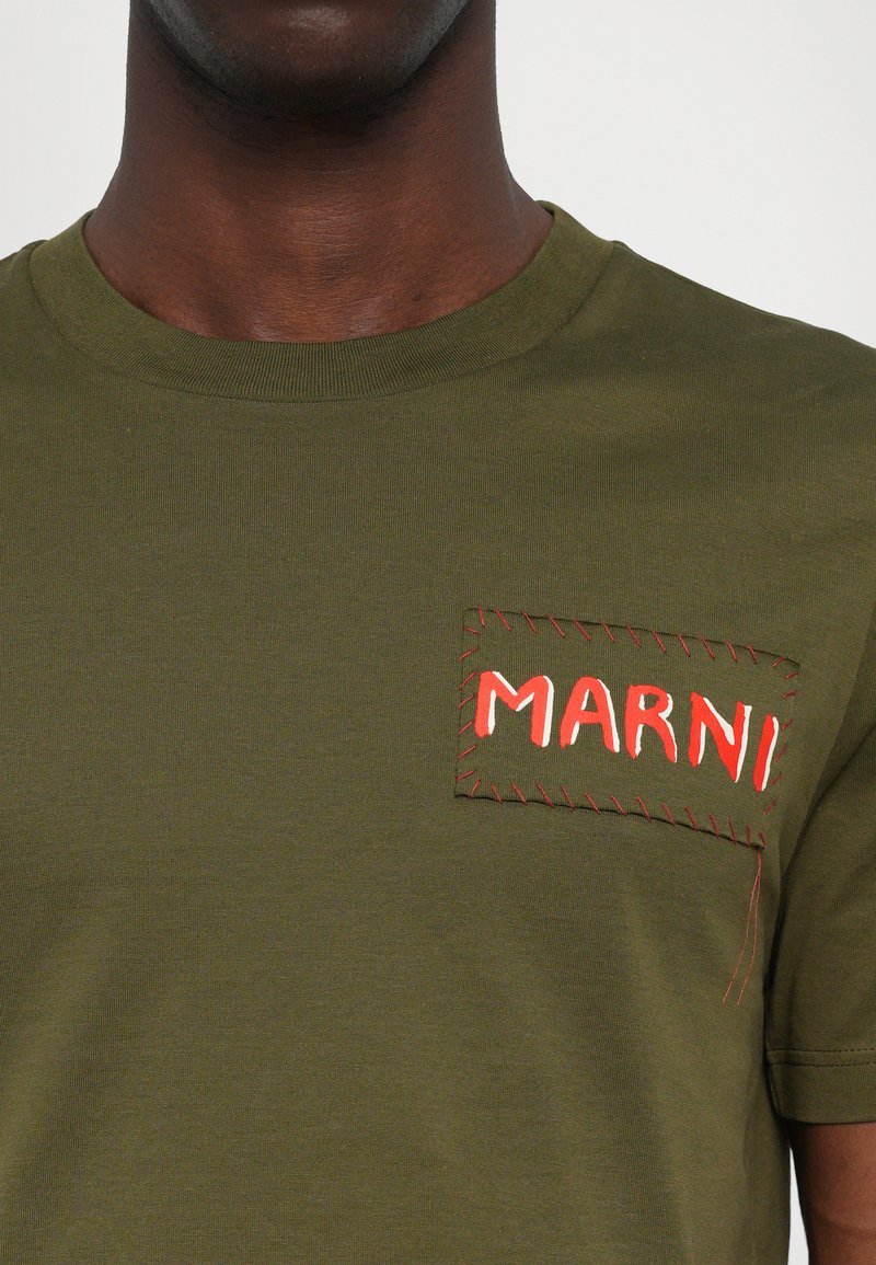 Camiseta de algodón verde oliva con un parche rectangular cosido en amarillo, con "MARNI" bordado en rojo. Diseño clásico de cuello redondo.