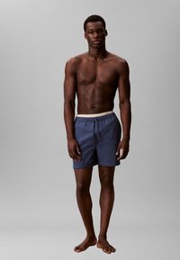 Pantaloni da bagno in tessuto blu scuro con vita elasticizzata e cordoncino. Design semplice, lunghezza a metà coscia, texture liscia.
