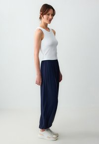 Top a righe bianco abbinato a pantaloni larghi blu navy, con una vita elastica. L'outfit è completato da scarpe da ginnastica bianche.