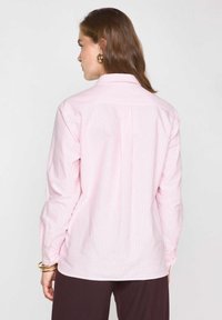 Chemise à manches longues en rose et blanc à rayures verticales, en tissu coton, avec des poignets boutonnés, un col classique, et un détail de empiècement au dos.