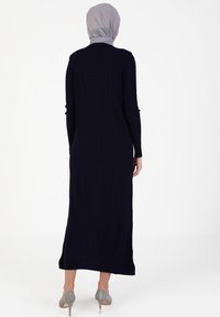 Navy ribbed long dress with long sleeves and a round neckline, featuring a smooth texture and a straight silhouette, paired with gray heels.