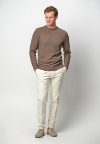 Maglione a maglia marrone, pantaloni crema e sneakers grigio chiaro. Design semplice, forma aderente, con polsini e orlo a coste. Nessun motivo o accentuazione visibili.