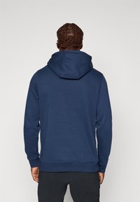 Marineblå hettegenser med snøring i hetten, ribbestrikkede mansjetter og kant. Laget av mykt stoff, med en glatt tekstur og et ensfarget design.