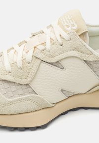 Beige- und cremefarbene Sneakers mit Wildleder-, Leder- und gewebten Stoffpaneelen, weißen Schnürsenkeln und einer gepolsterten Gummisohle.