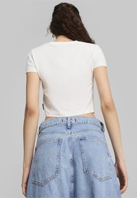 Afklippet hvid t-shirt med korte ærmer, parret med højdeskåret lys blå denimnederdel med knaplukning og to baglommer.