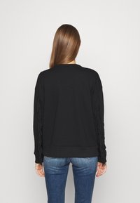 Černá mikina se třásňovým detailem na rukávech, kulatým výstřihem a volným střihem, v kombinaci s modrými džíny.