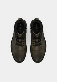 Zapatos de cuero verde oliva con puntera redonda, cordones negros y detalles texturizados. Presentan un collarete acolchado y plantillas de marca para mayor comodidad.
