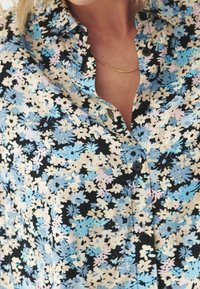 Košile na knoflíky s černým pozadím, zdobená květinovým vzorem v modré, růžové a bílé barvě. Měkká látka s límečkem a knoflíky.