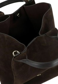 Borsa tote in suede marrone con manico in pelle nera liscia, caratterizzata da dettagli in metallo dorato e un design a scomparto aperto.