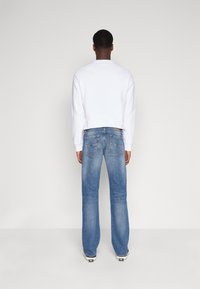 Sudadera blanca de cuello redondo combinada con jeans de campana de color azul claro. Los jeans cuentan con bolsillos traseros cosidos, y el modelo lleva zapatillas blancas.