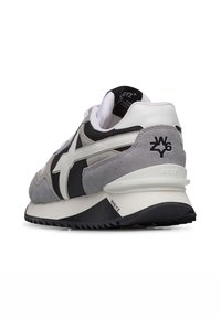 Sneaker grigio e nero con tomaia in suede e sintetico, caratterizzato da dettagli bianchi e suola in gomma testurizzata. Include il logo del marchio sul tallone.