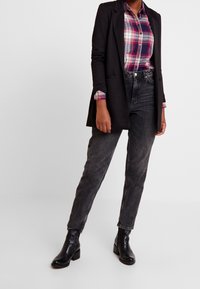 Black blazer over a plaid shirt in pink, purple, and white, paired with gray high-waisted jeans and black leather ankle boots.