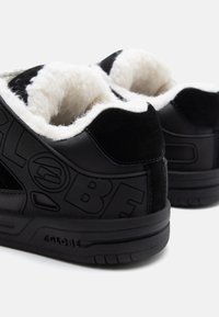 Black sneakers with a textured leather upper and white faux fur lining. Features embossed branding and a chunky rubber sole.