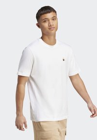 Hvid kortærmet t-shirt i bomuld med rund hals og en lille logo-patch på venstre bryst. Blød struktur og lige pasform.
