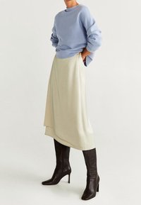 Suéter de punto azul, falda asimétrica color crema y botas marrones hasta la rodilla. Texturas suaves, con mangas relajadas y una silueta de falda fluida.