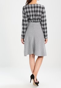 Haut à manches longues à carreaux noir et blanc associé à une jupe évasée grise. L'ensemble est complété par des chaussures à talons hauts noires.