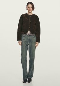 Brun fløjls crop jakke med rund halsudskæring og tre knapper, kombineret med falmede blå jeans med lige ben og sorte spidse støvler.