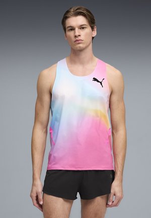 Giovane uomo che indossa una canotta multicolore senza maniche Puma e pantaloncini sportivi neri su sfondo grigio.