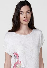Top blanc à manches courtes présentant un motif floral avec des fleurs brodées roses et violettes d'un côté ; tissu doux avec une coupe décontractée.