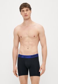 Mustade meeste bokserpüksid, millel on sinine elastne vöökoht, millel on "NIKE" bränding. Kangas on siledal ja keha vormi järgiv.