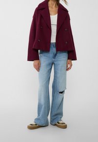 Bordowa, podwójnie zapinana, skrócona kurtka, szerokie niebieskie dżinsy z przetarciami oraz zielono-brązowe sneakersy. Posiada klasyczny kołnierz i zapięcie na guziki.