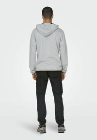 Sudadera gris con capucha ajustable, combinada con pantalones cargo negros y zapatillas deportivas multicolores, vista desde la parte trasera.