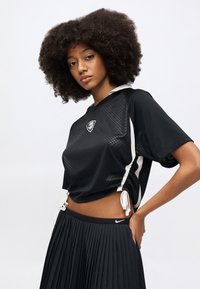 Μαύρο αθλητικό κοντό τοπ με υφή και λευκές πλαϊνές λεπτομέρειες, σετ με πλισέ μαύρη φούστα με λογότυπο στη μέση.