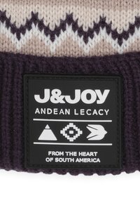Bonnet tricoté avec un revers côtelé violet, présentant un motif zigzag beige et blanc. Étiquette noire avec logo et éléments de design andins.