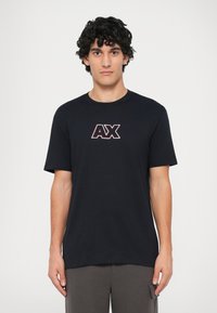 Camiseta de algodón negra con un logo central rojo y blanco "AX". Mangas cortas y cuello redondo. Textura suave, corte casual.