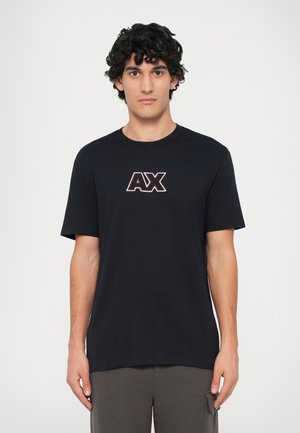 Camiseta de algodón negra con un logo central rojo y blanco "AX". Mangas cortas y cuello redondo. Textura suave, corte casual.